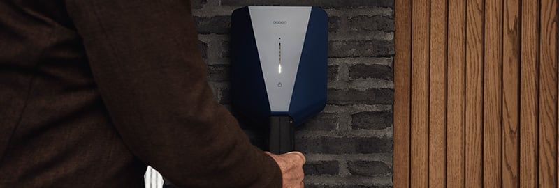 Person plugging in Easee One EV charger with sleek blue and grey design on brick wall